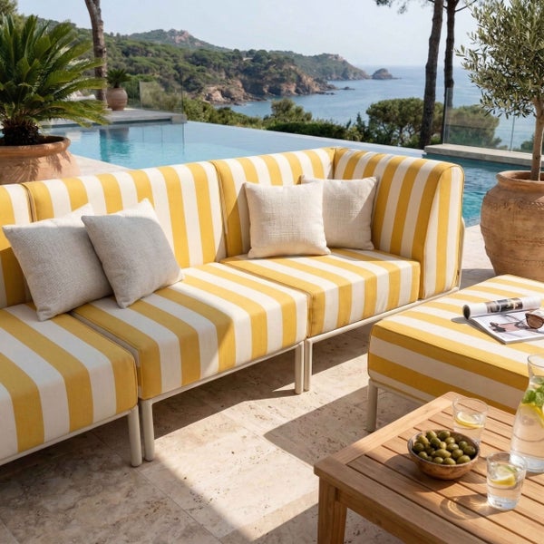 Moderne Outdoor-Lounge mit gelb-weiß gestreiftem Ecksofa, hellem Holztisch und Pool im Hintergrund auf einer sonnigen Terrasse mit Meerblick.
