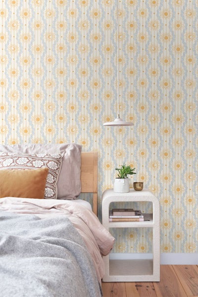 Vliestapete mit Sonnen- und Mondmuster im hellen Schlafzimmer hinter einem Holzbett und einem modernen Nachttisch.