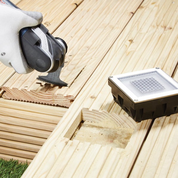 Installation einer Terrassenbeleuchtung mit Multifunktionswerkzeug in einer Holzterrasse.