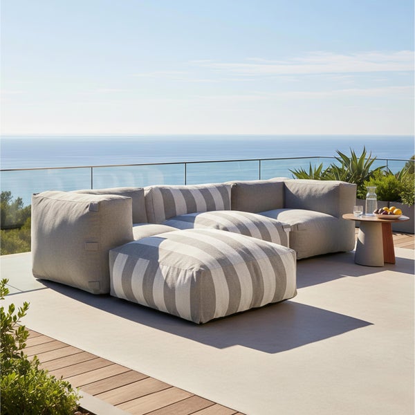 Moderne Outdoor-Lounge auf einer Terrasse mit Meerblick. Modulares Ecksofa aus grauen und grau-weiß gestreiften Polsterelementen.
