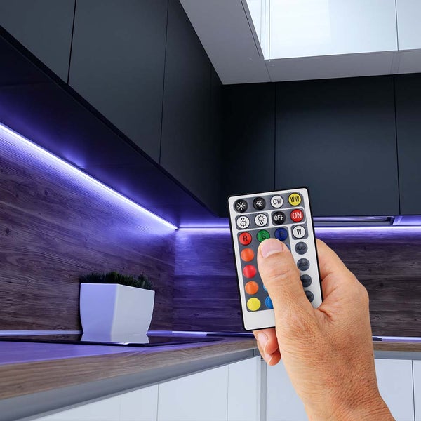 Küchenszene mit LED-Streifen unter den Schränken und einer Hand, die eine Fernbedienung hält