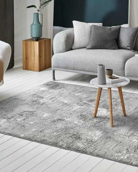 Heller, moderner Wohnraum mit grauem Teppich im Vintage-Muster, grauem Sofa und Marmor-Beistelltisch auf weißem Holzboden.