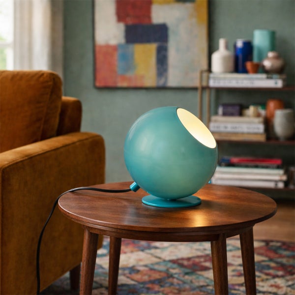 Moderne kugelförmige Tischleuchte auf einem runden Beistelltisch aus Holz in einem hellen Wohnzimmer mit Sofa und Regal.