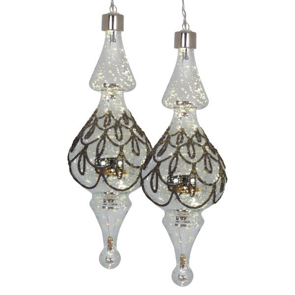 Zwei Glas Christbaumspitzen mit Ornamenten hängen an Fäden.