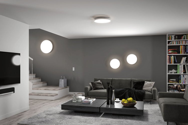 Modernes, organisiertes Wohnzimmer mit runden LED-Wand- und Deckenleuchten, grauem Sofa, dunklem Couchtisch und einer Treppe mit Holzstufen.