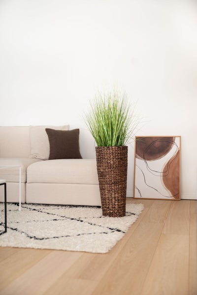 Modernes helles Wohnzimmer mit künstlichem Gras im hohen geflochtenen Korb neben einem Sofa und einem gemusterten Teppich.