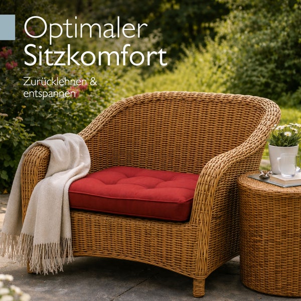 Gartensessel aus Korbgeflecht mit Sitzkissen und Decke neben einem Beistelltisch im Außenbereich