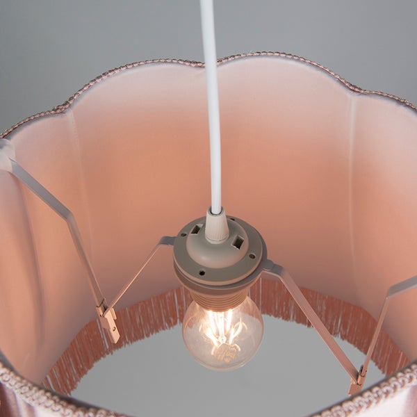 Innenansicht einer Pendelleuchte mit gewelltem rosa Stoffschirm, Fransen und leuchtendem LED-Leuchtmittel an einem weißen Kabel.