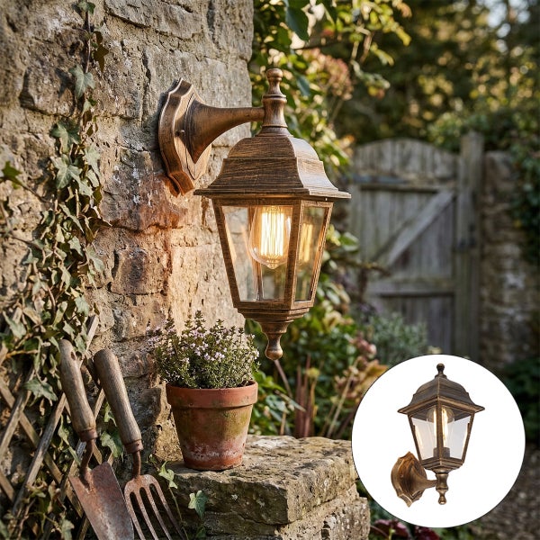 Klassische Außenwandleuchte im Laternen-Design aus Metall und Glas, montiert an einer Steinwand in einem hellen Garten.