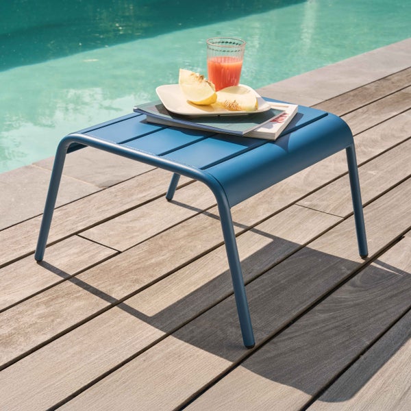 Blauer Beistelltisch aus Metall mit Lattenoberfläche auf einer Holzterrasse an einem Pool mit Getränk und Snack.