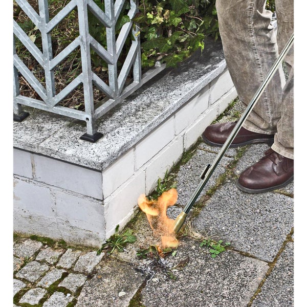Unkrautentfernung mit einem Gasbrenner auf Pflastersteinen neben einer Mauer