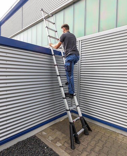 Mann steigt auf einer Teleskopleiter an einer Wand hoch.