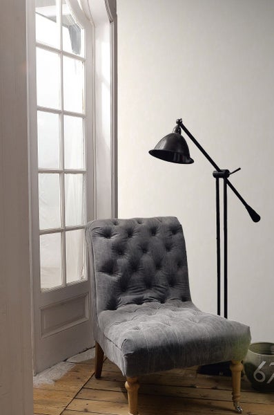 Grauer Sessel mit Knopfheftung neben einer Stehlampe