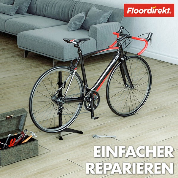 Szene mit Rennrad auf einem Montageständer, Werkzeugkasten und einem Schraubenschlüssel auf einem Holzboden