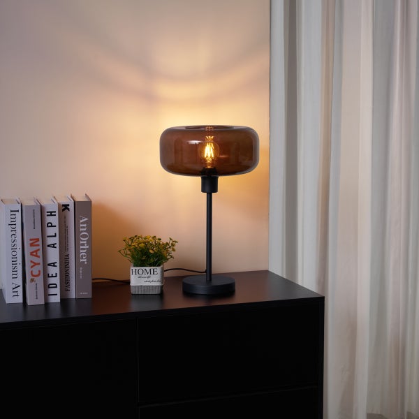 Dekorative Tischleuchte mit bernsteinfarbenem Glasschirm auf einem schwarzen Nachttisch