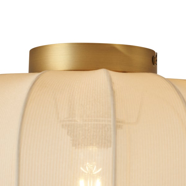 Nahaufnahme einer Deckenleuchte mit goldfarbener Halterung und cremefarbenem Textilschirm aus plissiertem Stoff.