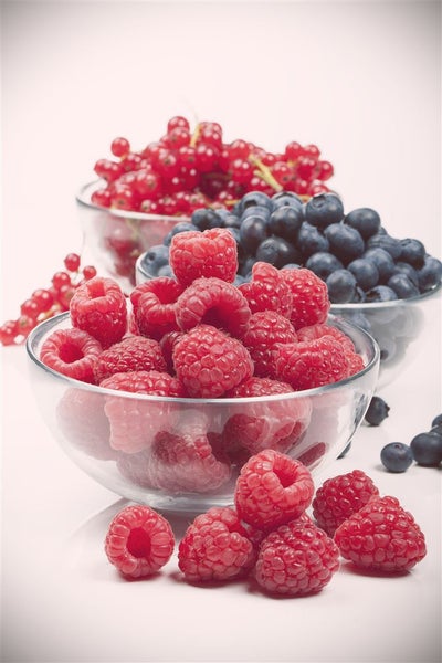 Drei Glasschalen gefüllt mit Himbeeren, Heidelbeeren und Johannisbeeren auf einer Oberfläche platziert.