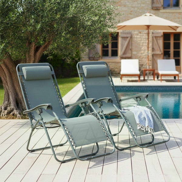 Zwei verstellbare Garten-Relaxliegen mit Kopfkissen auf einer hellen Holzterrasse am Pool neben einem Olivenbaum.