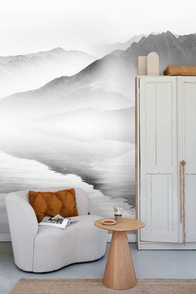 Wohnraum mit Sessel, Tisch und Schrank vor einer Fototapete mit Bergmotiv