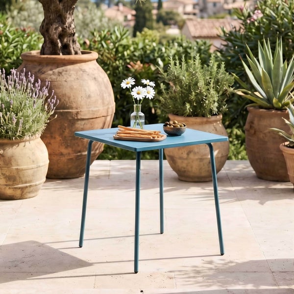 Quadratischer Gartentisch aus Metall in Blau auf einer hellen Terrasse, umgeben von großen Terrakottatöpfen mit mediterranen Pflanzen.