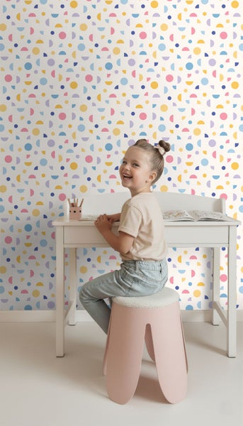 Vliestapete mit buntem geometrischem Muster aus Kreisen und Halbkreisen in einem hellen Kinderzimmer mit weißem Schreibtisch.