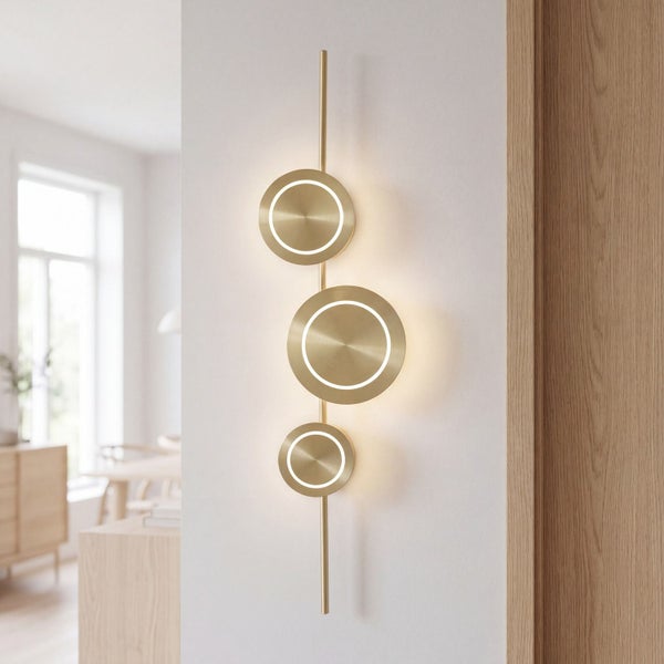 Moderne goldfarbene Wandleuchte aus Metall mit drei runden LED-Elementen an vertikaler Stange in hellem Zimmer montiert.