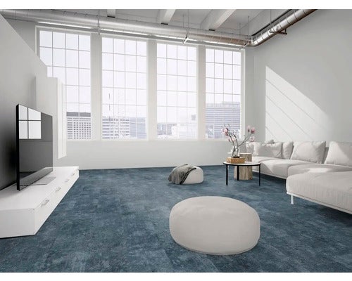Moderner Wohnbereich mit blauen Teppichfliesen, großem Sofa, hellen Fenstern und industriellen Deckendetails.