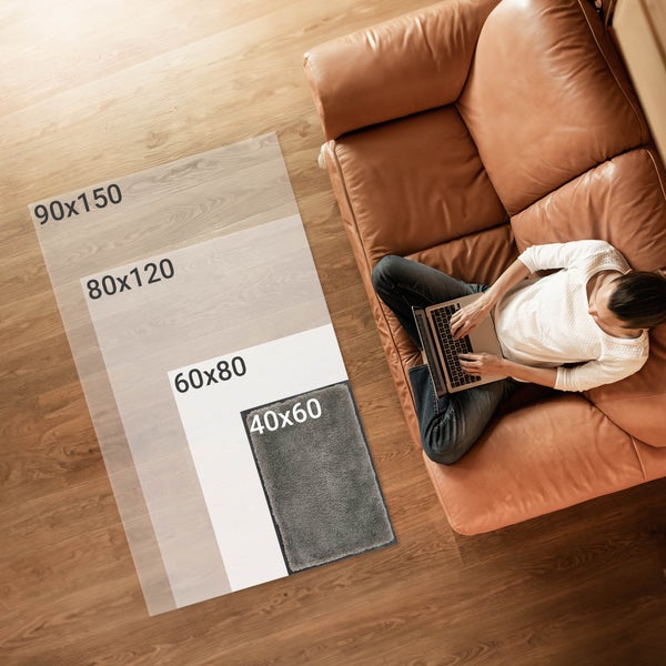 Verschiedene Teppichgrößen neben einer Person mit Laptop auf einem Sofa.