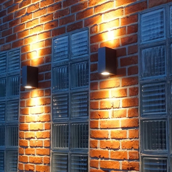 Moderne rechteckige Wandleuchten mit Up-and-Down-Beleuchtung an einer Ziegelwand mit Glasbausteinen.