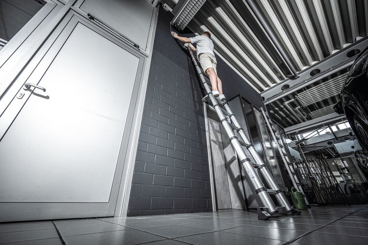 Mann auf einer Teleskopleiter, der an einer Wand arbeitet.