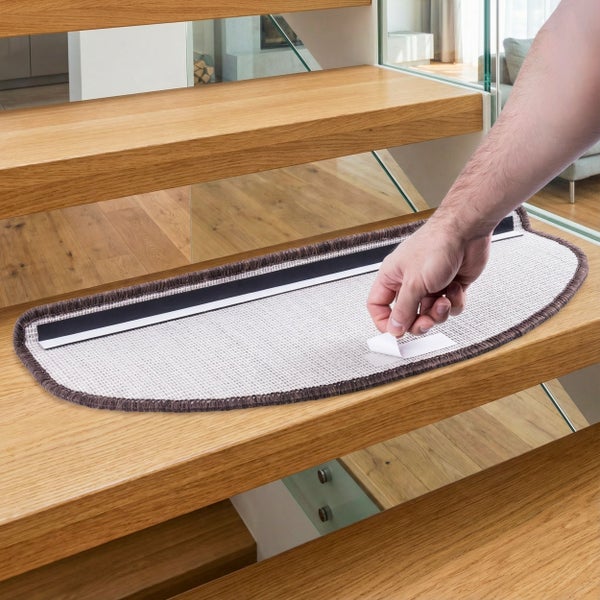 Eine Hand zieht die Schutzfolie von einer selbstklebenden Treppenmatte ab, die auf einer Holztreppe liegt.