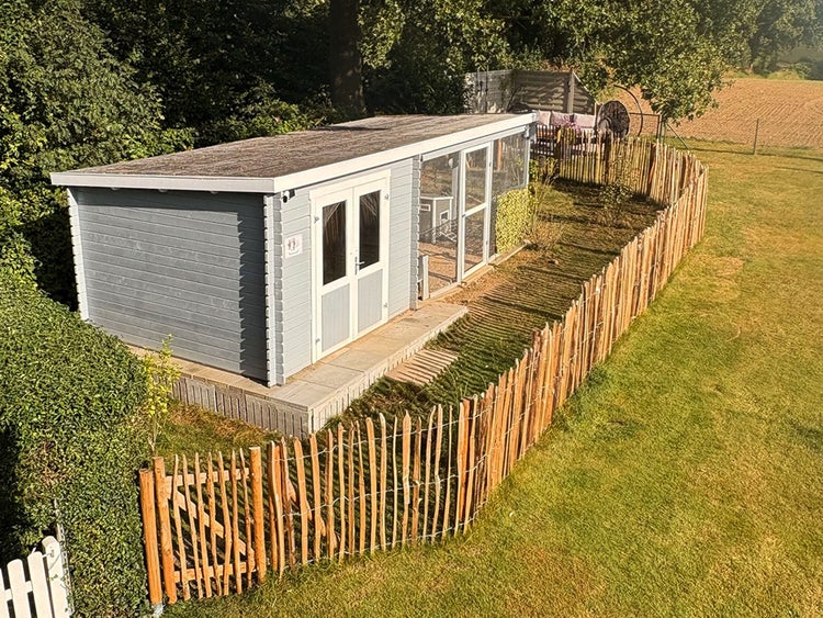 Gartenhaus mit integrierter Voliere und Pultdach, umgeben von einem Staketenzaun aus Holz auf einer Rasenfläche.