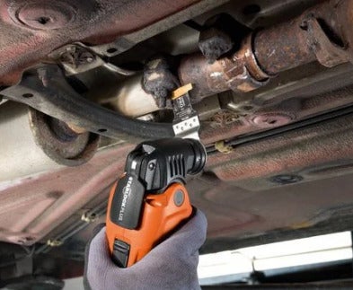 Ein handgehaltenes oszillierendes Elektrowerkzeug mit Starlock Plus Aufnahme schneidet an einem metallischen Auspuffrohr unter einem Auto.