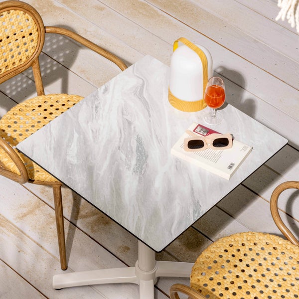 Quadratischer Gartentisch mit Platte in Marmor-Optik und zwei Bistrostühle mit Geflecht auf einer Holzterrasse.