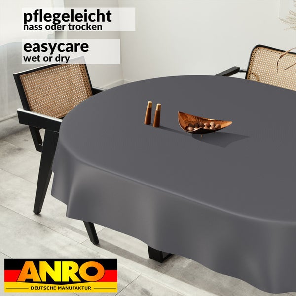 Runde, pflegeleichte Tischdecke in Anthrazit auf einem runden Tisch mit modernen Stühlen in einem hellen Raum. Anro Deutsche Manufaktur Logo.