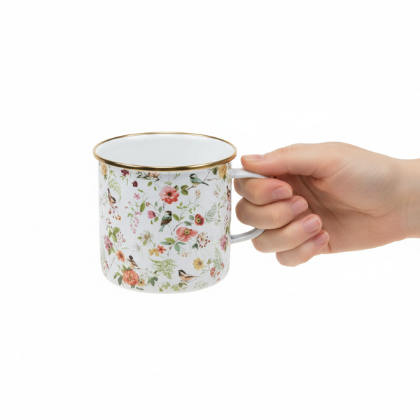 Hand hält einen Emaille-Becher mit Blumen- und Vogelmuster sowie Goldrand.