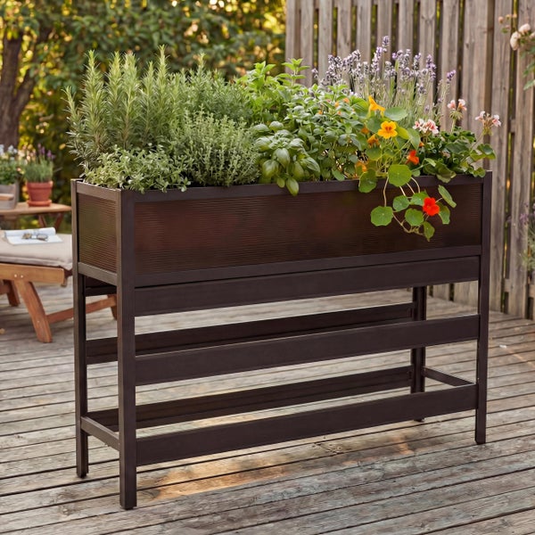 Modernes, dunkelbraunes Hochbeet aus Metall auf einer Holzterrasse, bepflanzt mit Kräutern wie Rosmarin und Basilikum sowie bunten Blumen.