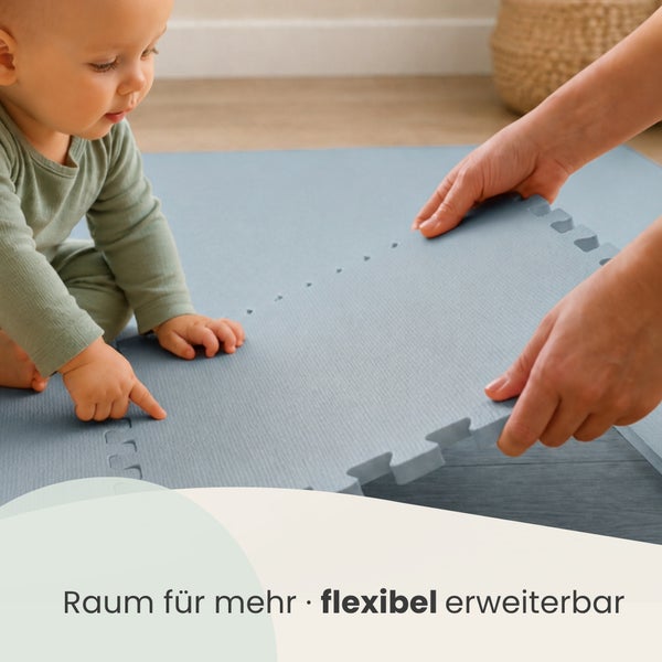 Ein Kleinkind spielt auf einer erweiterbaren Puzzlematte aus Schaumstoff, die durch ein Stecksystem flexibel zusammengesetzt werden kann.
