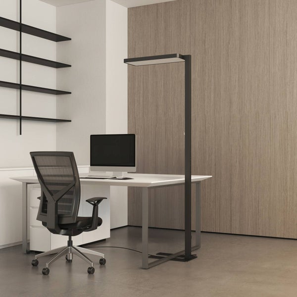 Modernes helles Büro mit weißem Schreibtisch, schwarzem Bürostuhl und schwarzer LED-Stehleuchte vor einer Wand in Holzoptik.