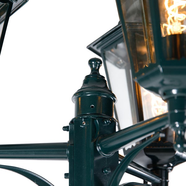 Nahaufnahme einer grünen Außenleuchte aus Metall im klassischen Design mit dekorativer Spitze und sichtbarem Leuchtmittel.