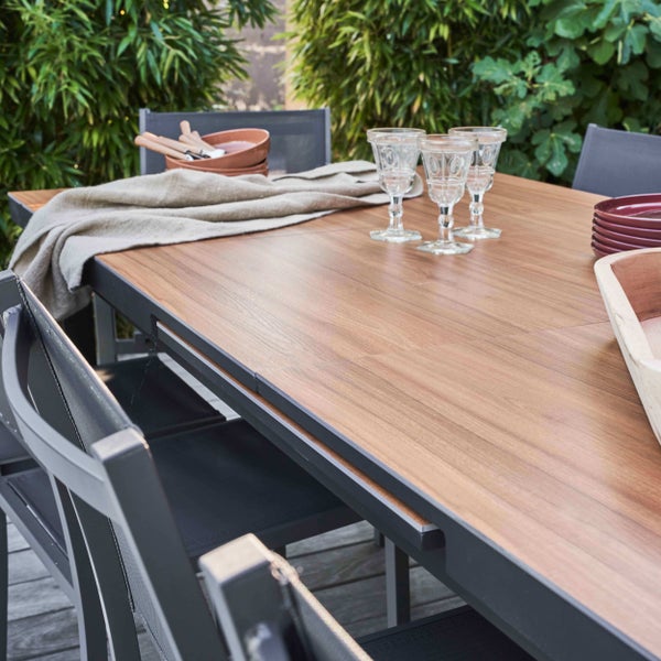 Ausziehbarer Gartentisch mit Tischplatte in Holzoptik und Metallgestell auf einer Terrasse mit Stühlen und Dekoration.