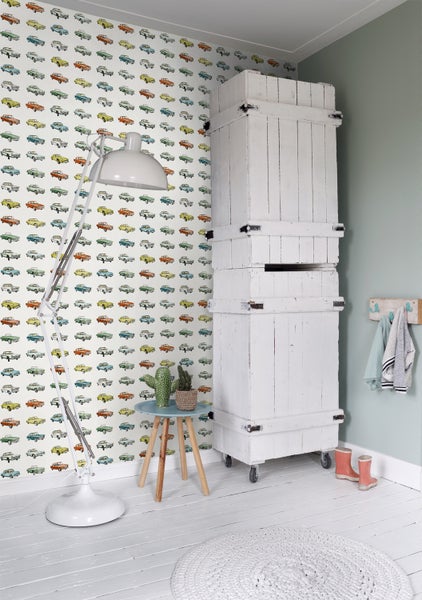 Heller Raum mit Oldtimer-Tapete, Stehlampe, kleinem Tisch und weißem Schrank auf Rollen
