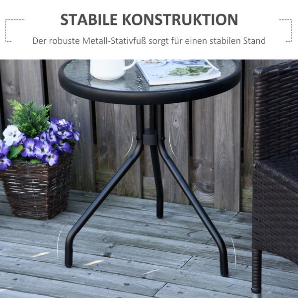 Runder Bistrotisch mit Glasplatte und stabilem Metall-Stativfuß auf einer Holzterrasse neben einem Blumenkorb und einem Korbsessel.