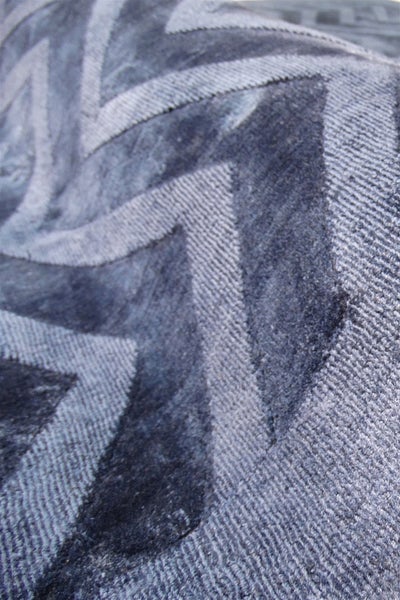 Nahaufnahme eines grauen Teppichs mit geometrischem Zickzack-Muster und kontrastierenden Texturen aus flauschigen und gerippten Oberflächen.