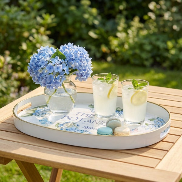 Ovales Serviertablett mit Blumenmuster, Hydrangea-Motiv, auf einem Holztisch mit Gläsern, einer Blumenvase und Macarons im Garten.