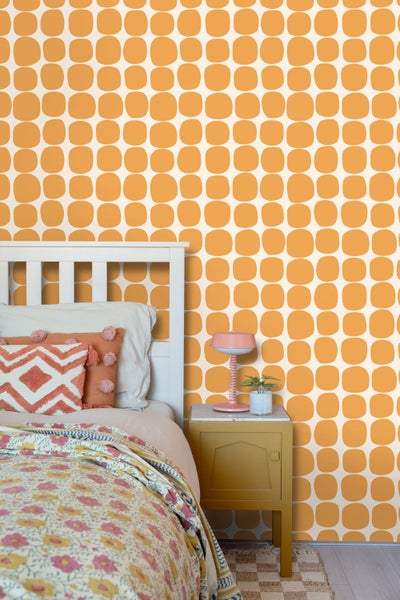 Tapete im Retro-Stil mit einem Muster aus abgerundeten Quadraten in einem hellen Schlafzimmer mit weißem Bett und gelbem Nachttisch.