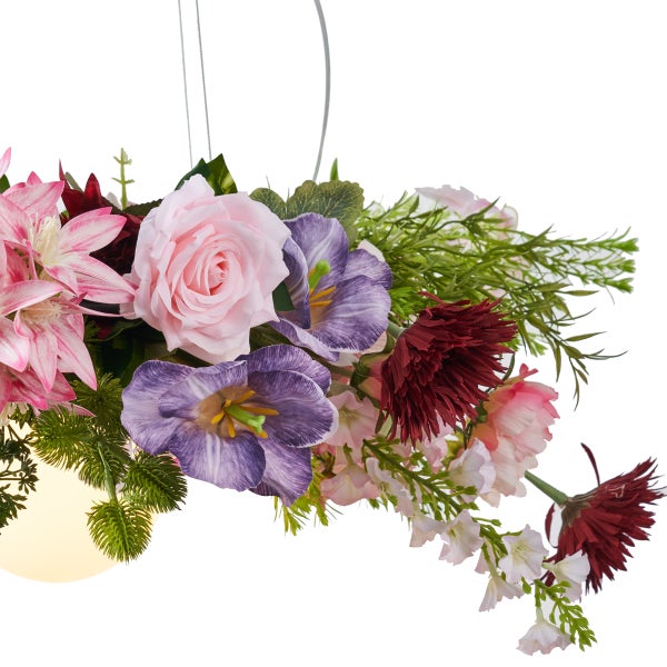 Künstliches Blumengesteck mit rosa Rosen, violetten Blüten und grünem Blattwerk.