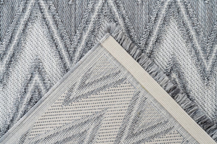 Detailansicht eines Teppichs mit Zickzack-Muster, die Webstruktur sowie die Rückseite und die gekettelte Kante zeigt.