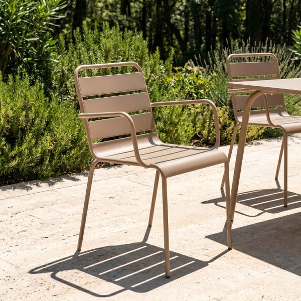 Beigefarbener Gartenstuhl aus Metall mit Armlehnen und Latten-Design auf einer hellen Steinterrasse im Freien.