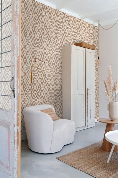 Wohnzimmer mit gemusterter Tapete, Sessel und Schrank